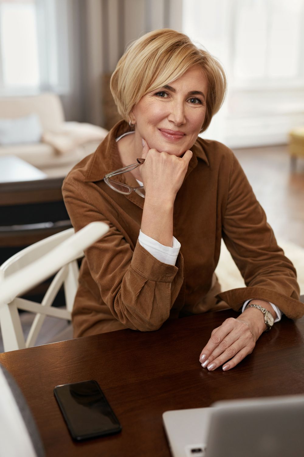 Smiling Dallas HBOT for plastic surgery woman sitting at a desk thoughtfully.