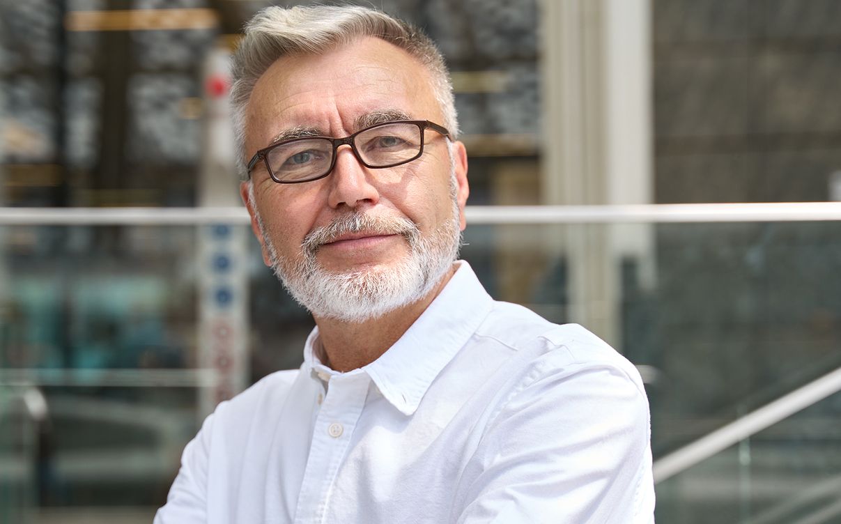 Older HBOT model with glasses smiling outdoors.